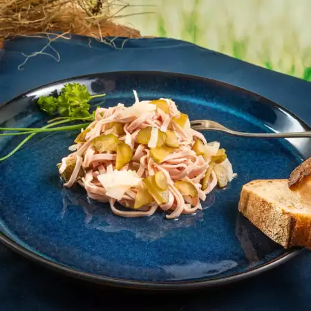 Wurstsalat auf blauen Teller mit Kräuter und Brot, Hintergrund grün