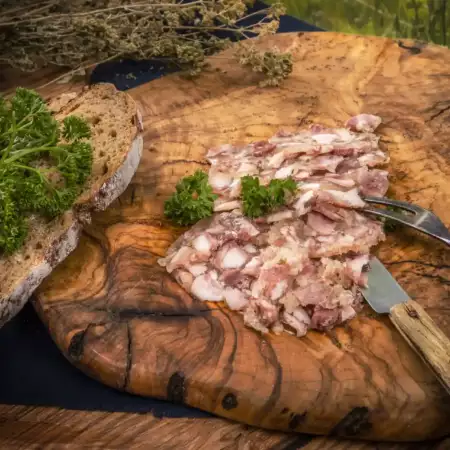 Pressack weiß essigsauer in Scheiben auf Holzbrett mit Brot und Kräutern und Besteck